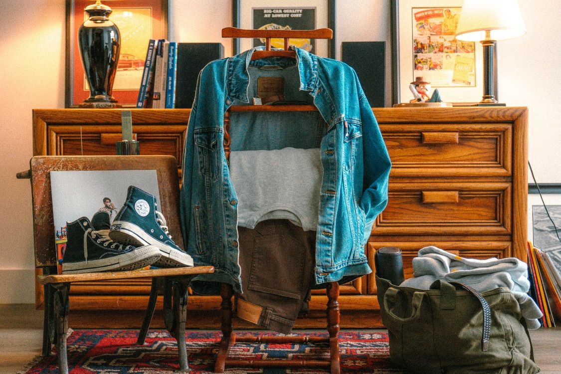 Denim jacket and packed bag styled on a vintage dresser