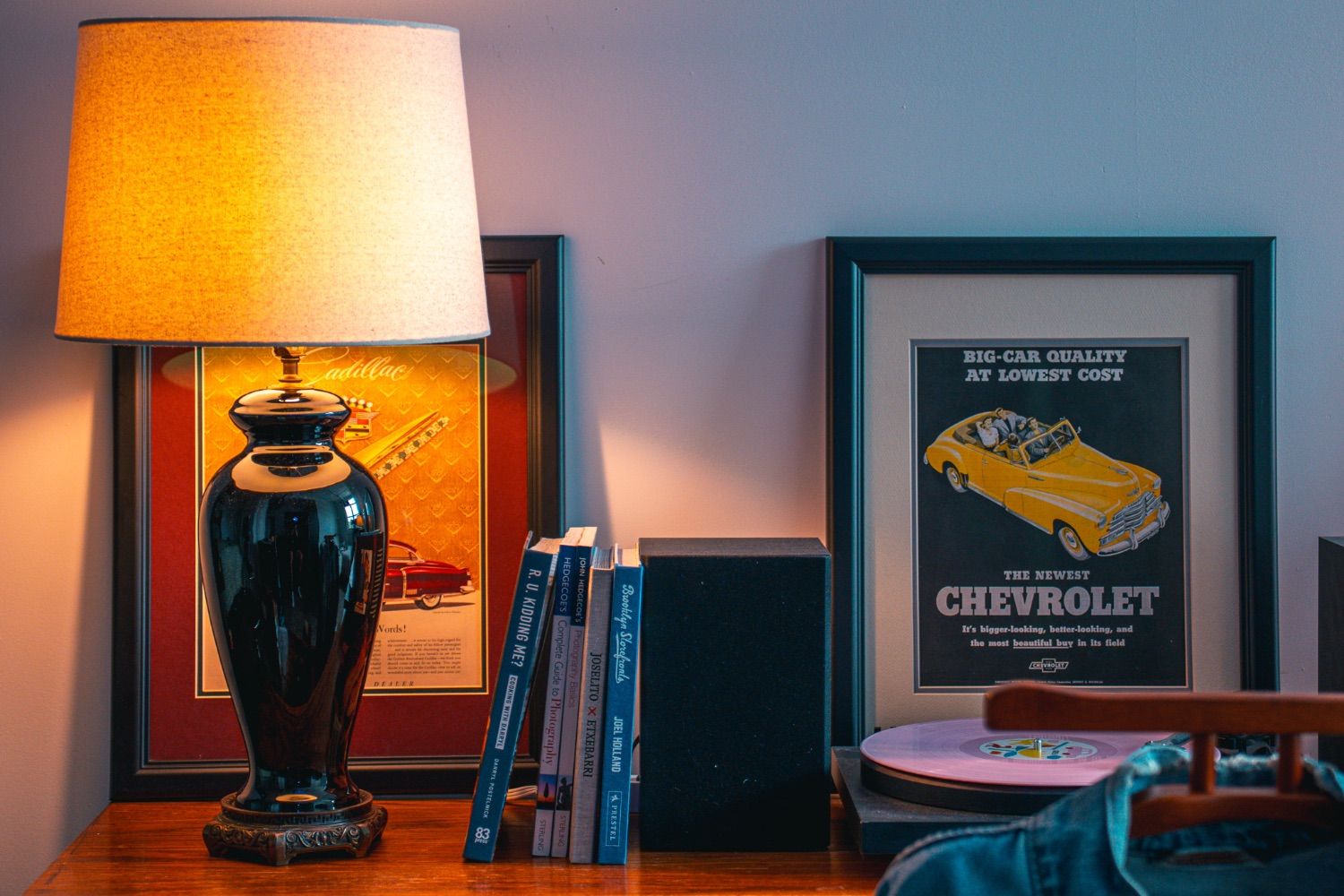 Vintage lamp, books, and framed car ads on a dresser